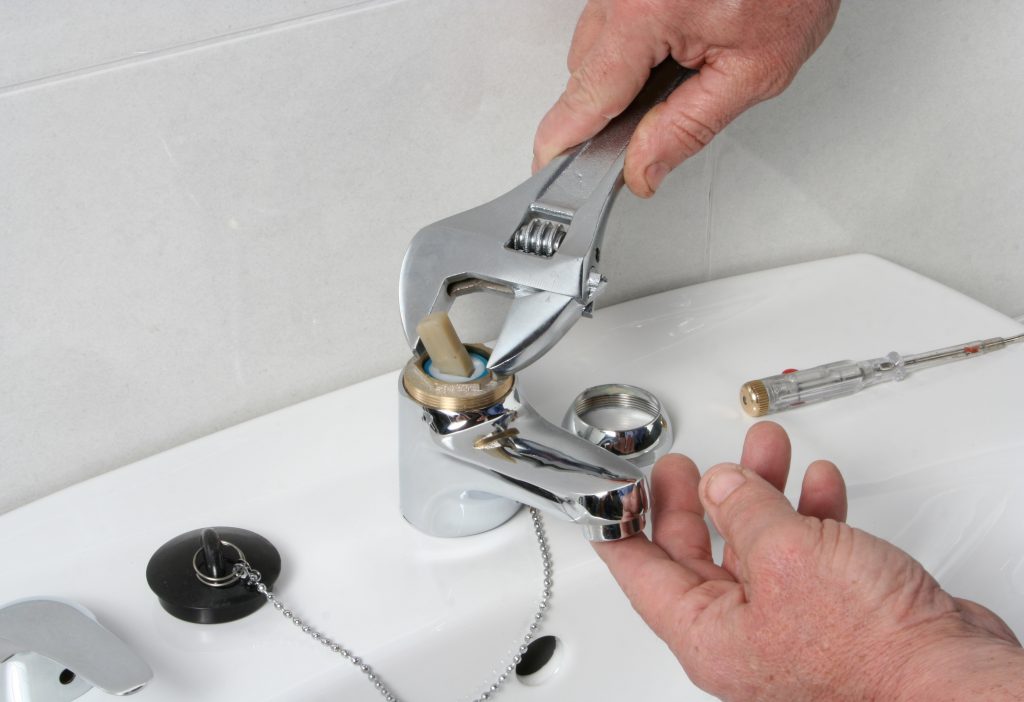 Man fixing a faucet using one of our suggested drain and plumbing hacks
